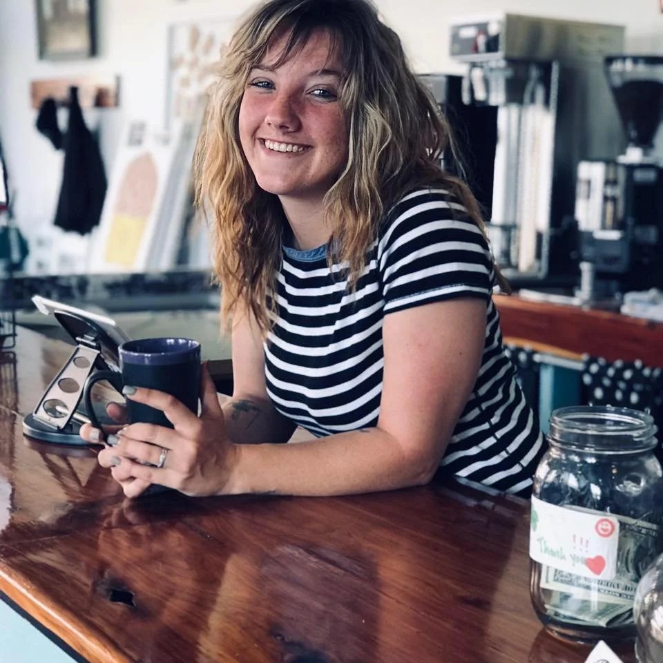 Amanda Pimenta smiling with a coffee mug at a café